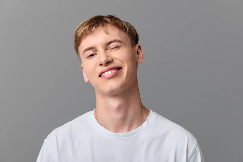 Smiling young man wearing a light tshirt against a neutral backdrop, relaxed pose and cheerful expression for lifestyle, wellness and positive messaging in marketing and social media
