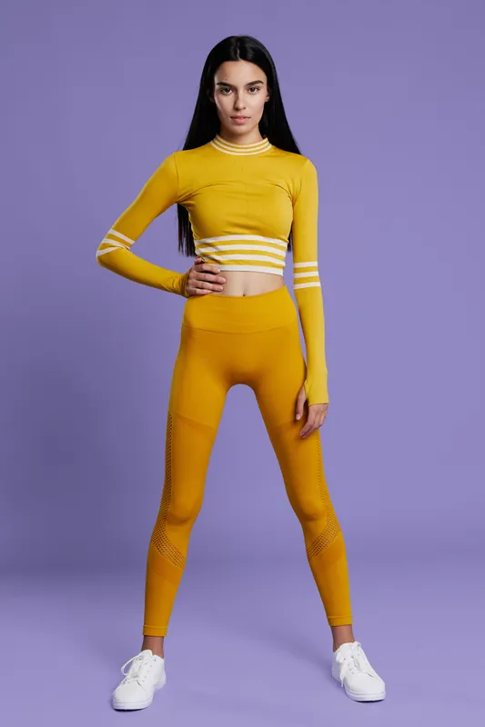 Woman sport fitness wearing yellow activewear stands confidently on violet background, showcasing health, energy, and modern athletic style for workout inspiration.