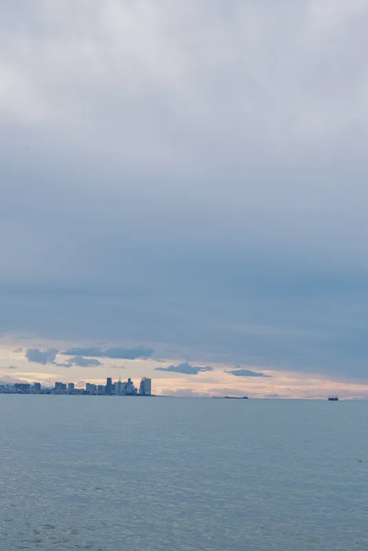 Calm sea and distant city skyline under a cloudy sky, wide water view with subtle horizon, tranquil coastal landscape ideal for travel, nature, and serene stock imagery.