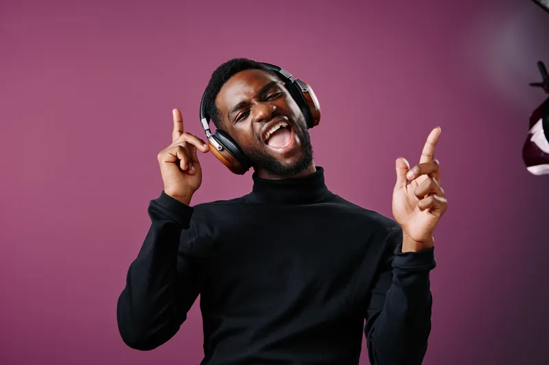 A joyful Black man in a black turtleneck and headphones dancing to music against a vibrant purple background, embodying happiness, rhythm, and enjoyment