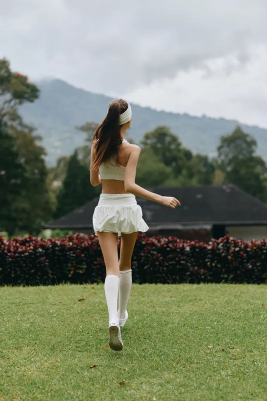 Young athletic woman in white sportswear running in nature, showcasing a sense of freedom and vitality amid lush greenery and a vibrant landscape