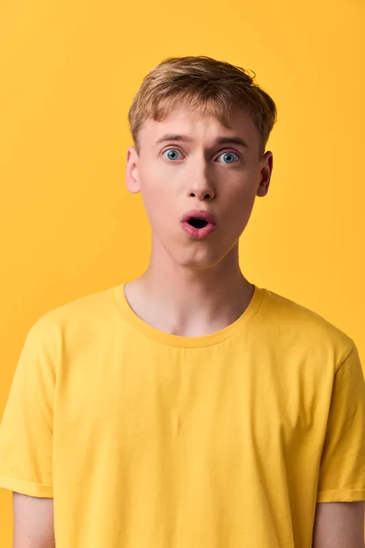 Surprised, astonished expression on a young man wearing a yellow tee against a bright backdrop, casual fashion and expressive studio shot for branding use
