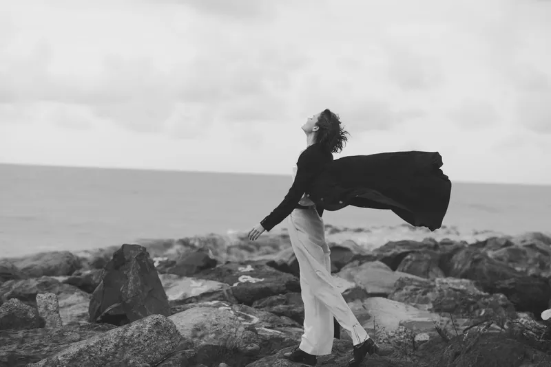 wind cape ocean coastline woman freedom motion dramatic landscape sea breeze on rocky shore monochrome mood windblown cape lifts with stride conveying liberation and exploration in a powerful seaside
