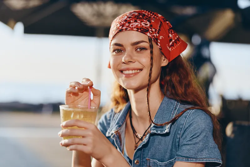 lifestyle woman in modern boho-western denim street style smiling with drink outdoors with film color tone lighting and casual summer vibe