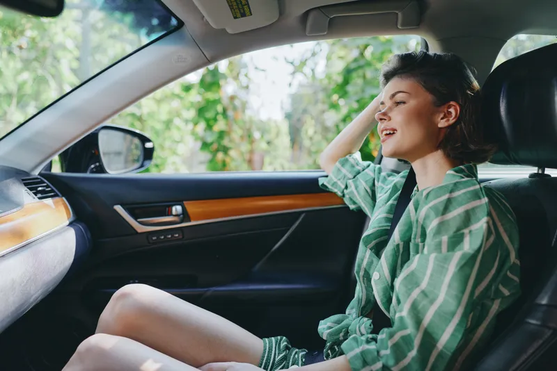 A woman sits in the driver's seat, smiling, enjoying a calm drive inside a sunlit car interior.