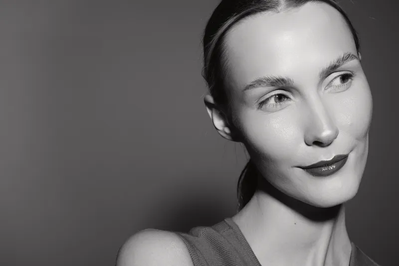 Portrait of a white young woman with light skin looking sideways with a subtle smile against dark background. Concept of natural beauty and confident expression.