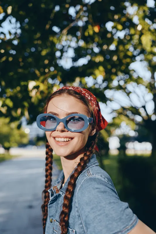 lifestyle woman in modern boho-western denim street style smiling outdoors with blue sunglasses and red bandana, vibrant film color background