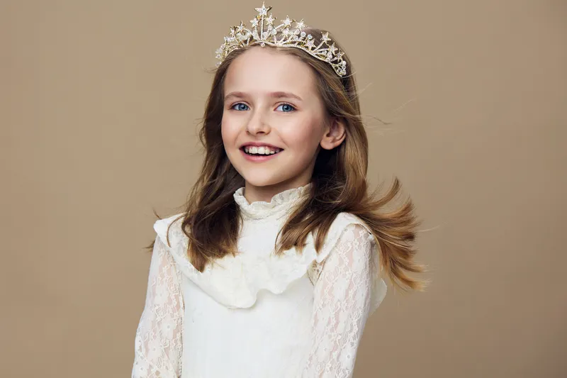 Smiling girl wearing a crown, showcasing joy and innocence against a neutral background, perfect for themes of childhood and celebration