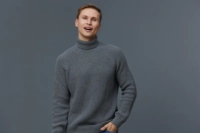 Happy smiling man wearing cozy grey sweater looking at camera pose casual relaxed indoor background portrait. People lifestyle concept.