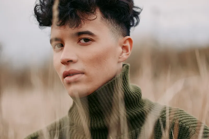 An authentic portrait with a candid gaze in soft natural light; a calm, genuine moment highlighted by a knitwear sweater and muted outdoor tones.