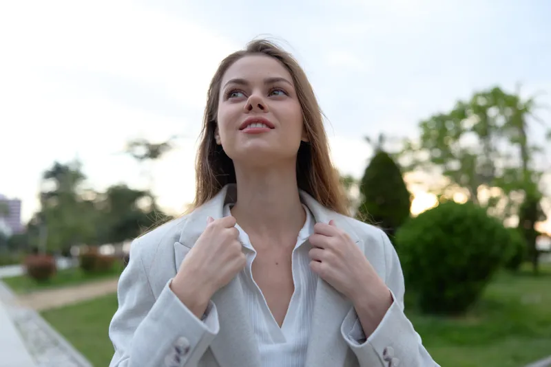 confident woman in gray blazer outdoors smiling with soft natural light and green park background in spring season