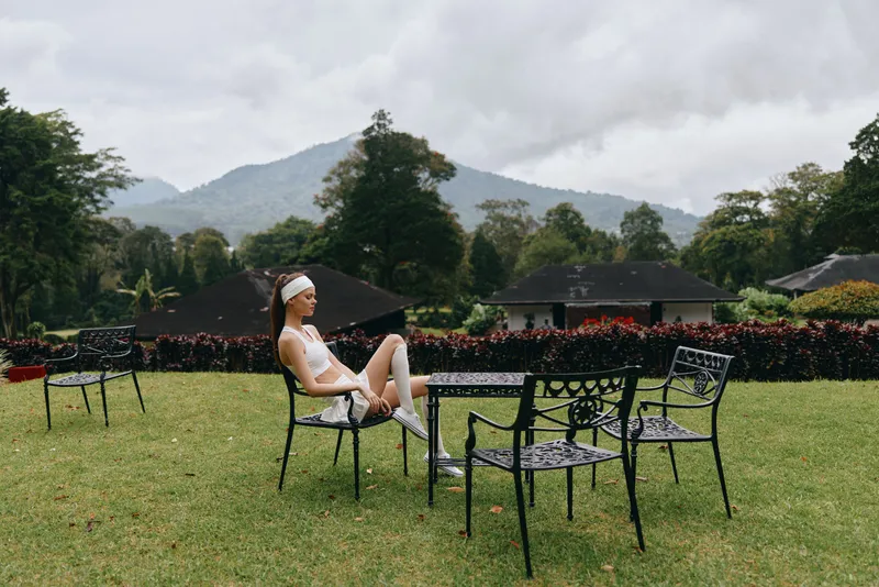 Young athletic woman relaxing outdoors in sportswear, enjoying nature and serenity in a modern garden setting, surrounded by green hills and cloudy skies