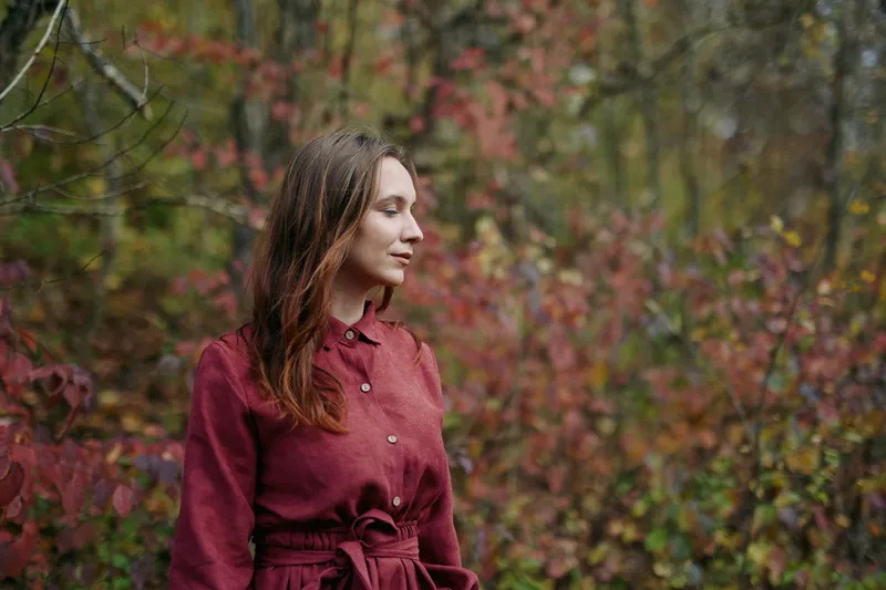 A candid portrait of a woman in a burgundy dress in an autumn forest, radiating authenticity and credibility under soft, natural light, with a calm, focused gaze.