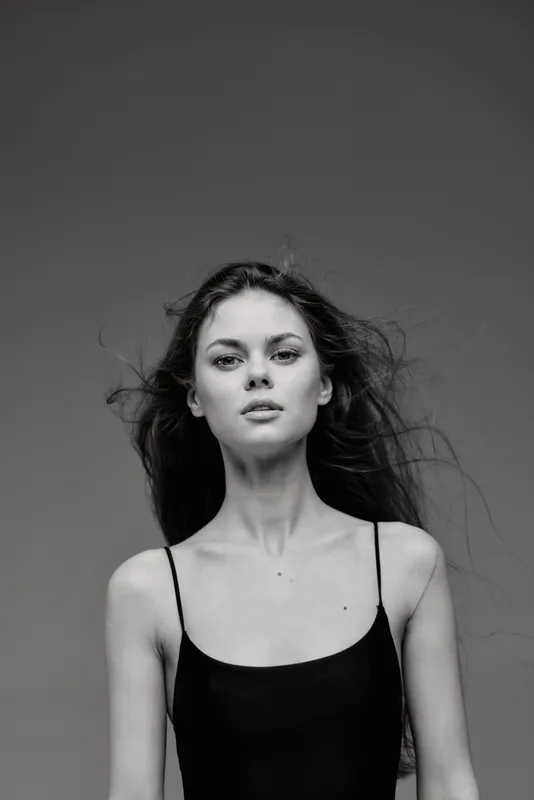 Black and white portrait of a young woman with flowing hair wearing a black tank top looking confident
