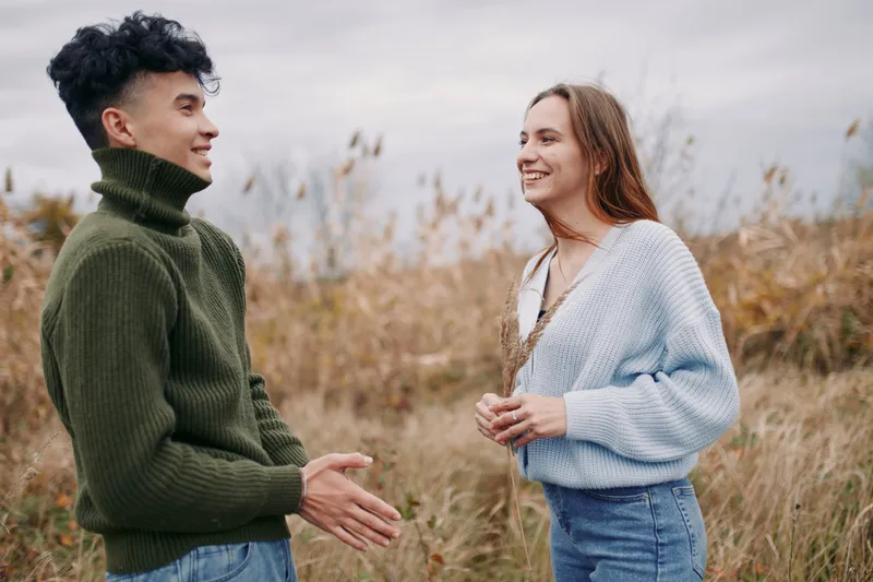 An authentic moment between two smiling friends outdoors, capturing genuine connection and candid interaction in soft autumn light across an open field.
