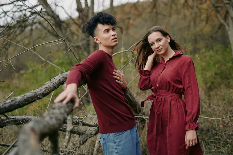 An authentic candid duo stands among autumn trees, captured in soft natural light with relaxed pose and genuine expression, conveying credible connection.