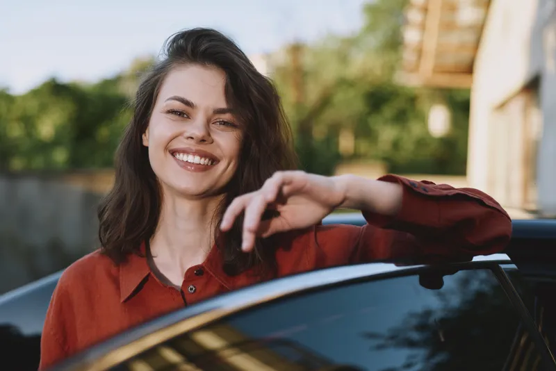 Vibrant woman lifestyle scene outdoors, smiling beside a car, sunlit moment with relaxed pose, natural colors, soft breeze, candid portrait of confidence