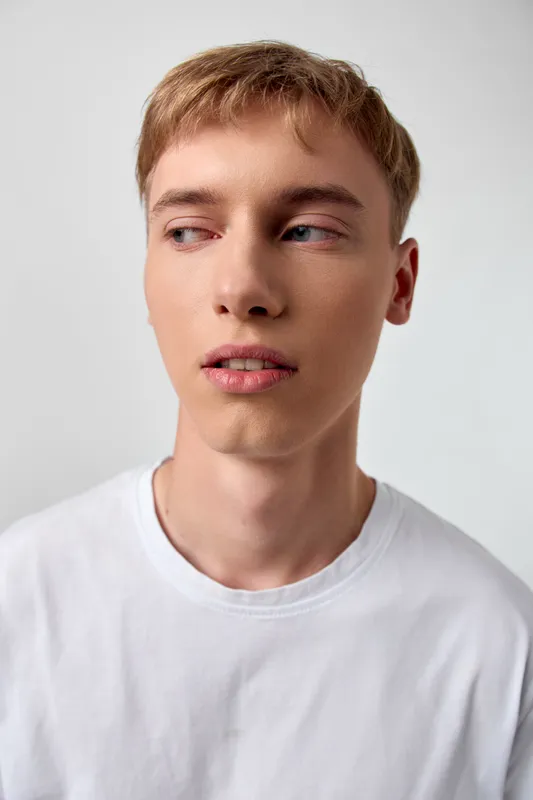 Youth, man, casual, thoughtful, closeup, white shirt, gaze, studio style, close framing of a young man looking away against a neutral backdrop with soft natural light highlighting calm expression