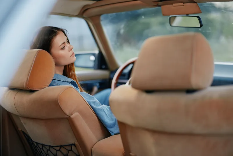 A young woman sitting in a vintage car, lost in thought, captures a moment of nostalgia and reflection with soft lighting and a serene expression.