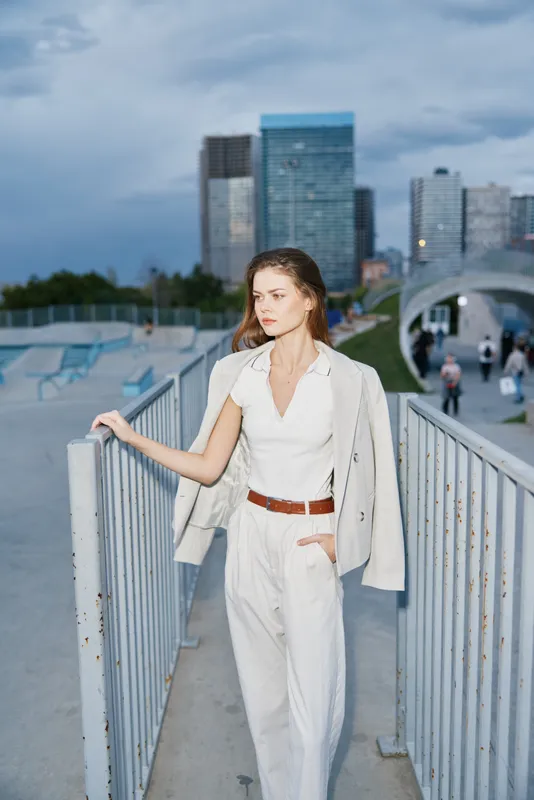 business woman in white outfit standing outdoors with modern city background and confident expression