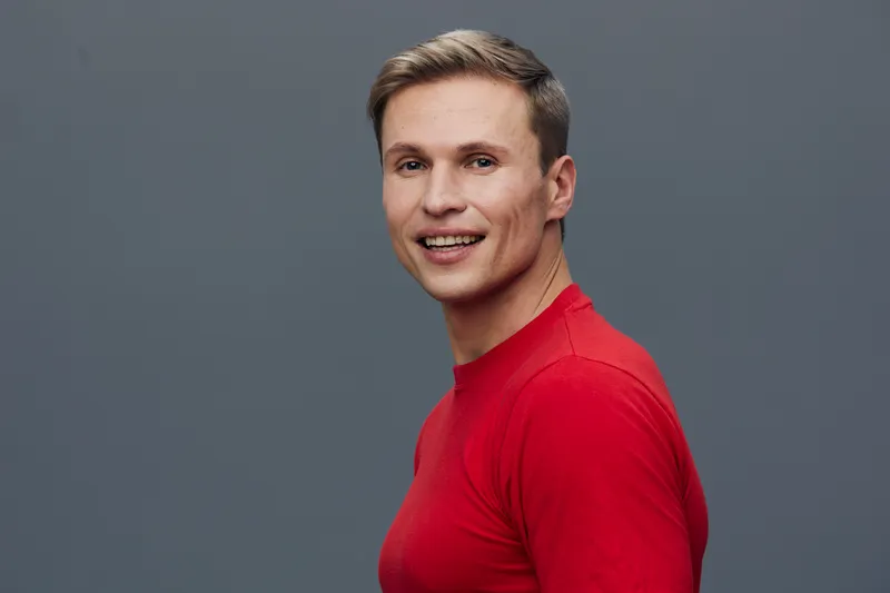 Smiling man with short brown hair wearing casual red t-shirt looking at camera studio portrait on gray background. People lifestyle concept
