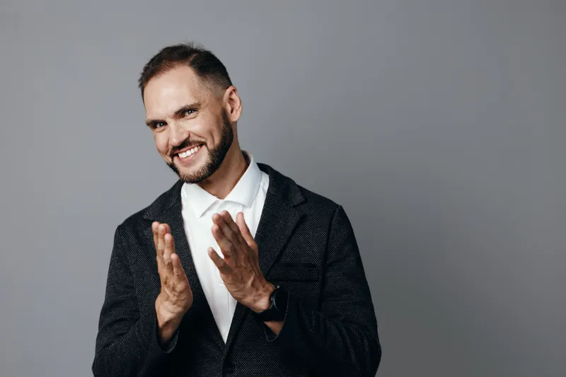 A confident businessman on an isolated gray background, dressed in a dark blazer and white shirt, exudes friendly energy and positive professional emotion.