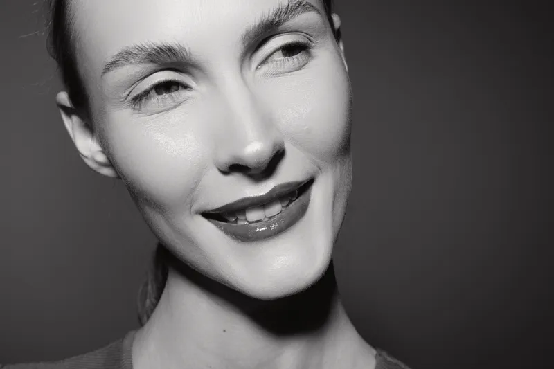 Close-up portrait of a smiling caucasian woman with fair skin and red lips against a dark background. Concept for beauty, happiness, and natural facial expression.