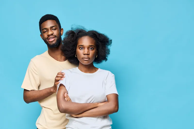 Two stylish young individuals standing against a blue background, showcasing modern fashion and diverse emotions, ideal for lifestyle and relationship concepts