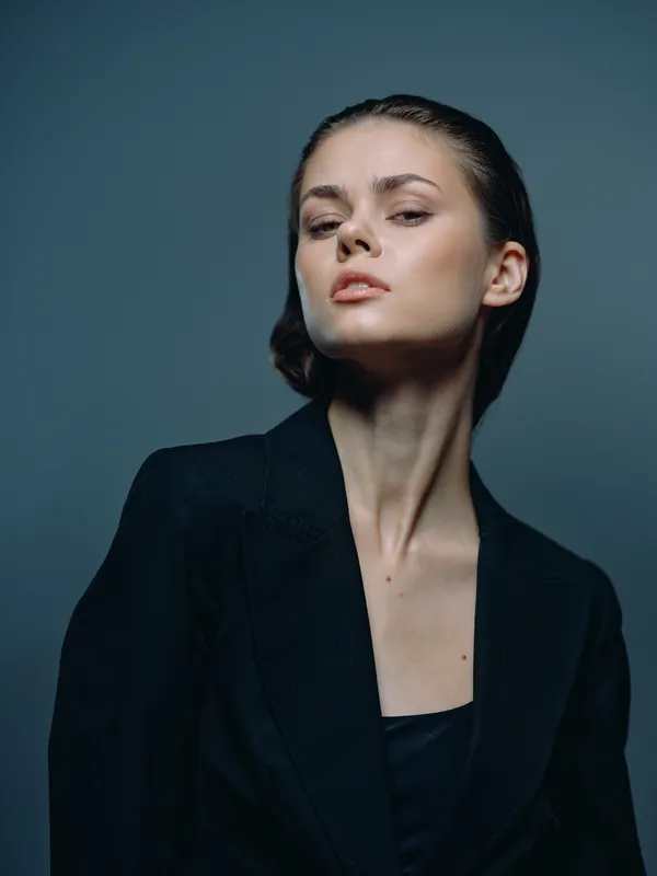 Confident woman in black blazer with serious expression on gray background, stylish and professional look.