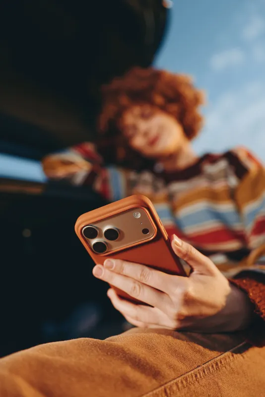 Woman holding smartphone at home lifestyle, parenting with family, blurred child resting on couch, communication and leisure, warm indoor light, cozy casual clothing, close portrait focus on device