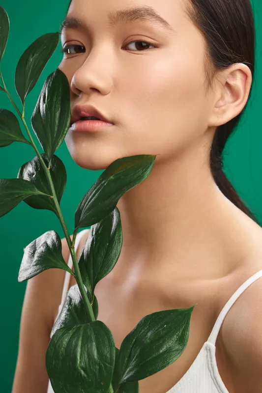 asian woman gazes softly amid lush leaves against a vivid green backdrop, creating a calm, natural portrait that emphasizes simplicity, balance, and contemporary wellness for a fresh, tranquil mood.
