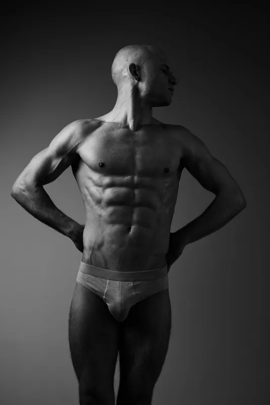 Black and white portrait of a muscular man showcasing strength and confidence, with striking shadows emphasizing his physique and form.