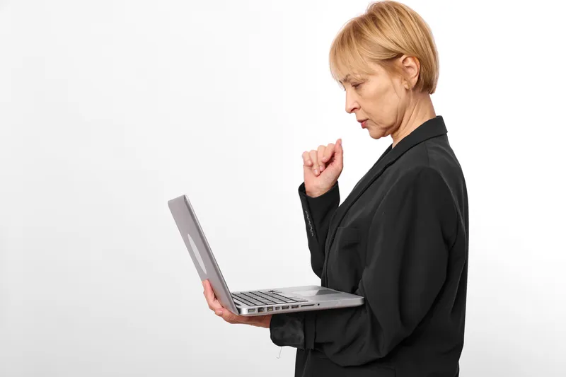 Businesswoman with laptop in studio, white background, profile view, stress expression, hand raised in gesture, focused on typing, black jacket, soft minimal lighting, bright