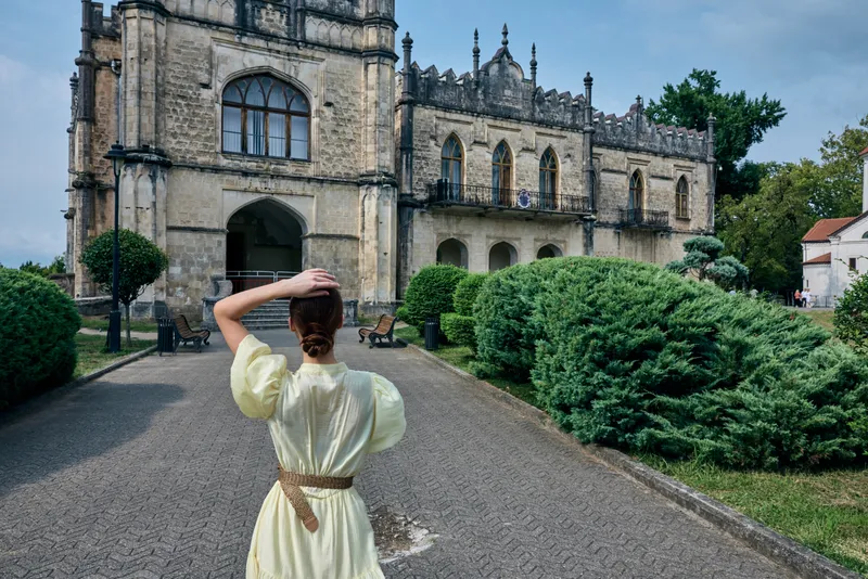 woman historic architecture garden walking backview dress authenticity inclusivity traveler exploring old building and shrubs