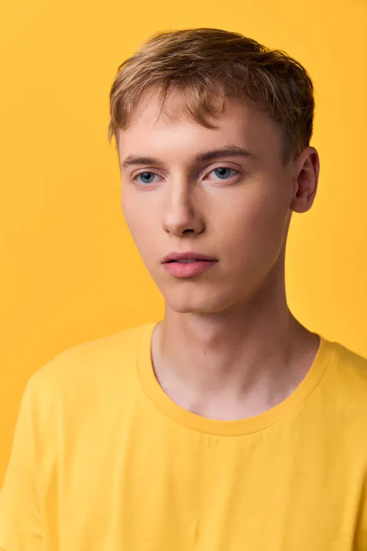 Young man in a yellow tee against a vibrant yellow backdrop, calm expression, clean studio lighting, minimalist setup, ideal for fashion, lifestyle and creative branding