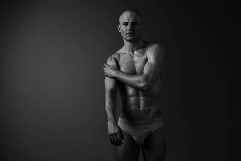 Black and white image of a confident man showcasing his toned physique. The dramatic lighting accentuates his strong features, conveying strength and determination.