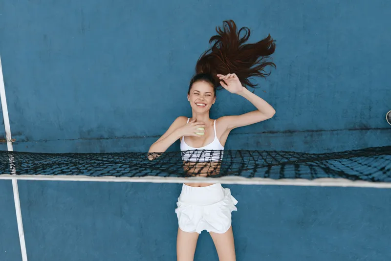 Happy young woman enjoying a sunny day while playing tennis, wearing a white sports outfit, against a vibrant blue background that enhances her joyful expression and active lifestyle