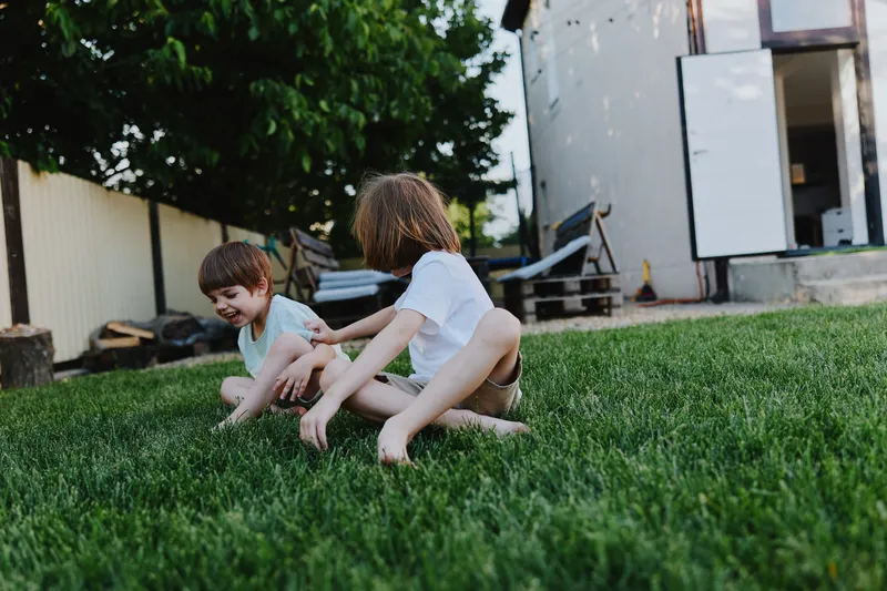 Playful children enjoying a sunny day, smiling and laughing in a grassy backyard, capturing moments of joy and innocence in nature.