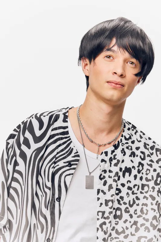young man wearing black and white animal print shirt and silver necklaces, modern hairstyle, looking confident on white background, stylish fashion portrait