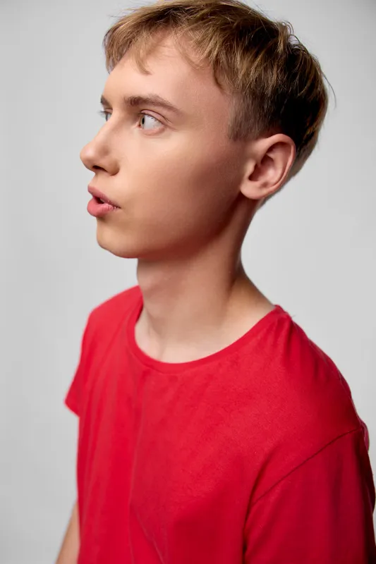 Close up of a male in a red shirt, side profile, thoughtful expression, with studio lighting against a plain background for a clean, casual and modern shot, minimal composition, headshot feel, color