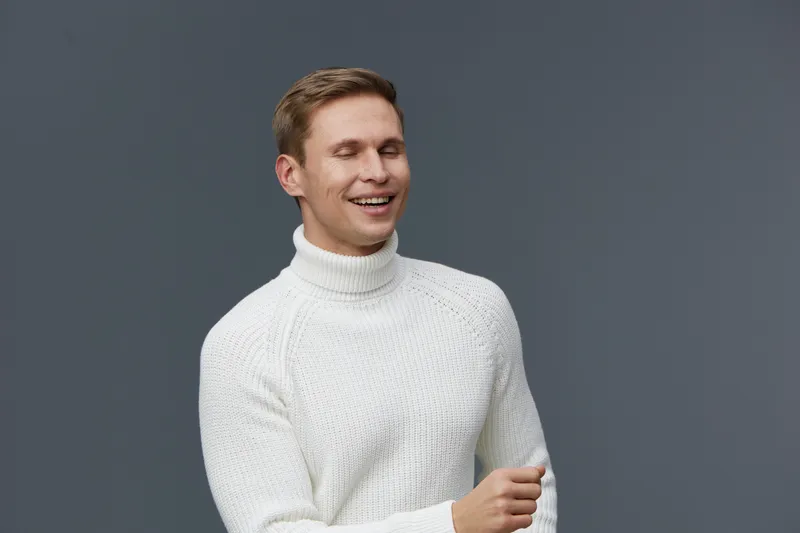 Smiling happy man in white sweater looking away isolated on plain gray background studio portrait. People lifestyle concept