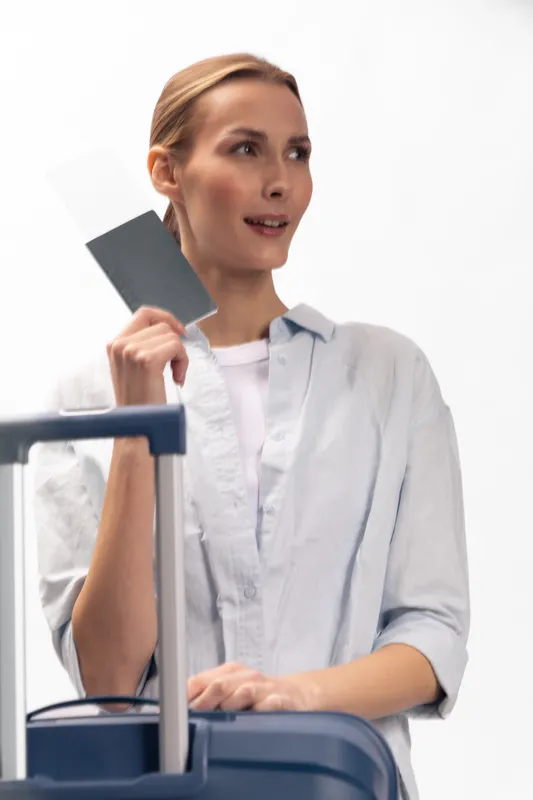 Young woman traveler holding passport and boarding pass near suitcase on white background. Concept of travel, vacation, and airport security check for tourism and transportation.
