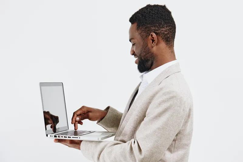 Professional man with dark skin using a laptop computer, working or browsing, isolated on white background, studio shot. Business technology concept, modern digital device, workplace productivity, pro