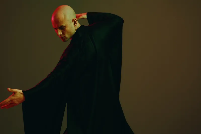 Captivating man in flowing black garment poses dramatically, showcasing elegance and emotion with subtle hints of light and shadow.