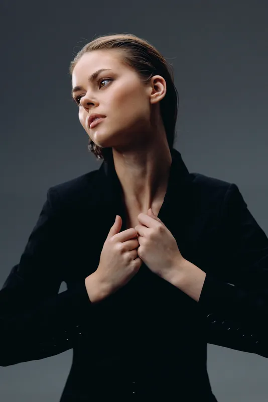 Thoughtful woman in black jacket looking aside with calm expression in studio setting