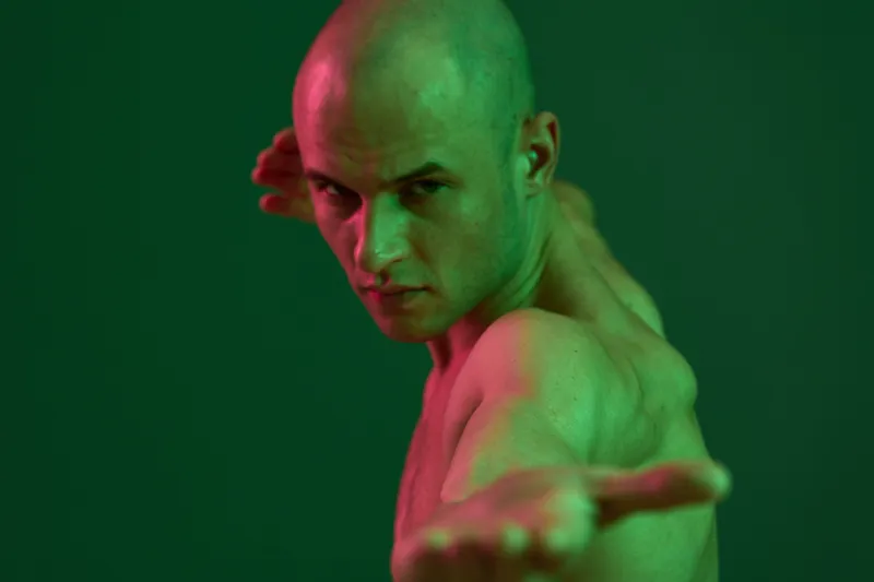 A strong man in a green light striking a dynamic pose, showcasing determination and strength. The vibrant colors highlight his muscular physique and intense focus.