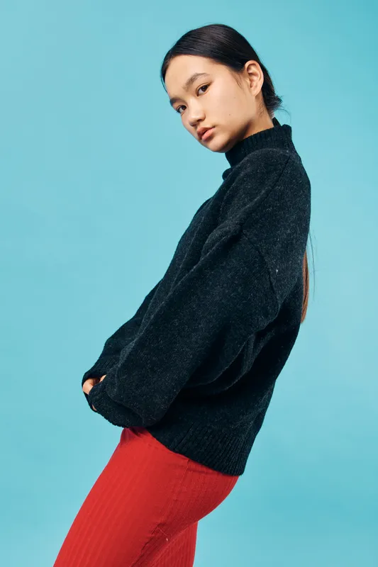 Young woman posing in black sweater and red skirt against blue background with serious expression, casual fashion style, studio portrait with minimalistic look and natural makeup.