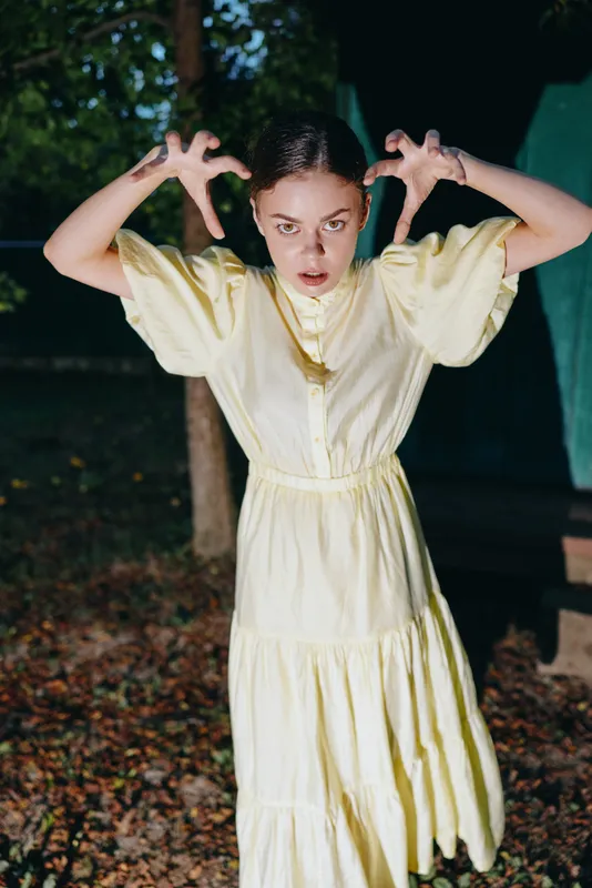 girl in yellow dress making spooky hand gesture at night outdoors, portrait with authenticity inclusivity and theatrical emotion