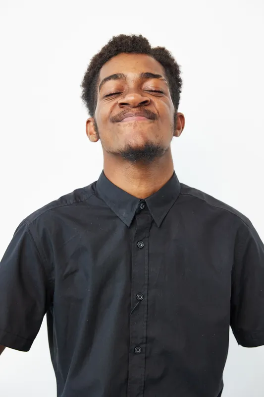 Happy African American man smiling confidently, dressed in a black shirt, showcasing a joyful expression against a clean white background, radiating positivity.