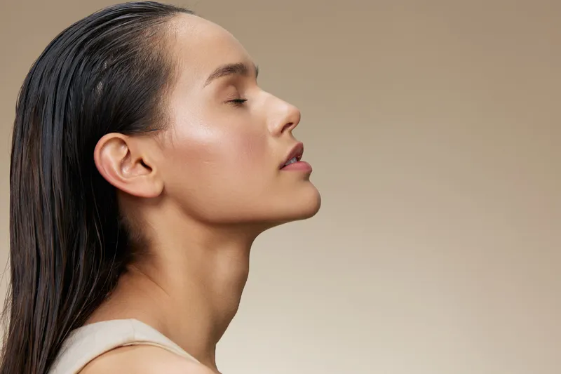 Serene young woman with long hair, showcasing natural beauty in soft lighting against a neutral background, evoking feelings of calmness and elegance